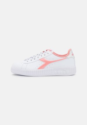 Zapatilla blanca de corte bajo con detalles en rosa, cordones y cuello acolchado, con suela texturizada y detalle de logo lateral.