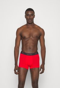 Boxer da uomo rossi in cotone con una fascia in vita nera con il marchio Calvin Klein, caratterizzati da un design aderente e una texture liscia.