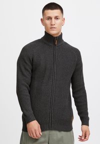 Dunkelgrau, gerippter Strick-Zipfelpullover mit hohem Kragen, kontrastierendem Reißverschluss und einem Lederpatch-Detail am Saum.
