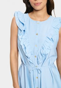 Rochie bleu deschis cu un decolteu volanat, închidere cu nasturi pe partea din față și o accentuare cu cordon la talie. Realizată dintr-un material moale, cu o textură netedă.
