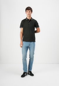 Crna polo majica s bijelim detaljima, uparena s svijetloplavim trapericama i crnim tenisicama. Majica ima ovratnik i kratke rukave.