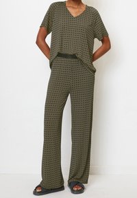 Conjunto de dos piezas que incluye una blusa de manga corta y corte holgado, y pantalones de pierna ancha. Tejido de color verde oscuro con un sutil patrón circular en toda la superficie.