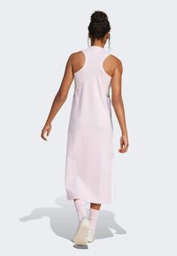 Rochie fără mâneci, de culoare roz pal, cu o formă alungită, fante laterale, textură subtilă. Asortată cu adidași albi și șosete roz. Vedere din spate.