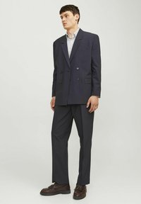 Marineblauer, doppelt geknöpfter Blazer mit großen Knöpfen, kombiniert mit passenden Hosen und einem gestreiften Hemd. Texturiert und tailliert.