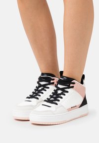 Höga sneakers med vit läderöverdel, svarta snören och rosa accenter; texturerad svart häl och vadderat ankelskydd.