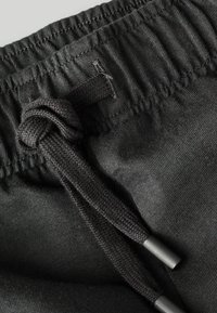 Pantalones negros con cordón ajustable y cintura elástica, que presentan un cordón trenzado anudado y una textura de tela suave.