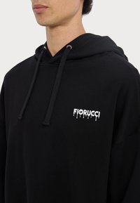Schwarzer Hoodie mit Kordelzug, der ein weißes "Fiorucci"-Logo auf der Brust trägt. Hergestellt aus einem weichen Material mit lockerer Passform und minimalistischem Design.