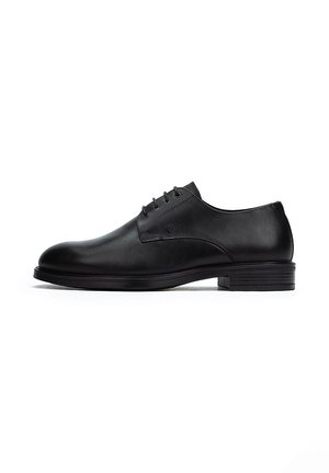 Zapato de cuero negro con punta redonda, seis ojetes, textura suave y un tacón de goma bajo. Diseño minimalista con acentos sutiles.