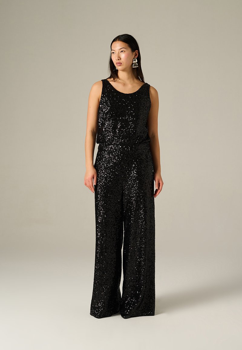 Jumpsuit noir en sequins avec design sans manches, pantalons évasés et encolure ronde. Texture lisse et surface brillante avec une taille cintrée.