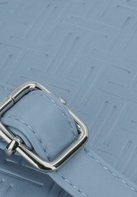 Borsa in pelle azzurro chiaro con un motivo geometrico testurizzato, dotata di una fibbia in metallo argentato e finiture lisce vicino all'area della tracolla.
