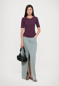 Purple fitted short-sleeve shirt, light blue denim skirt with a front slit, and a small black handbag with hardware accents. Striped wedge sandals.