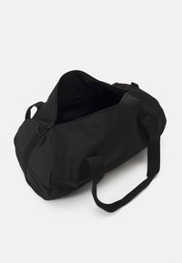 Sort duffelbag af kraftig nylon. Har en lynlåslukning, justerbare stropper og et rummeligt indre uden synlige mønstre eller metaldele.