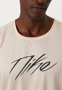 Helles Pfirsich-farbenes Mesh-Sportshirt mit rundem Halsausschnitt und schwarzem "Nike"-Logo in Schreibschrift auf der Vorderseite. Strukturierter, atmungsaktiver Stoff.