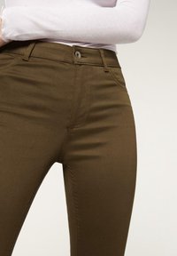 Jeans marrones ajustados con una textura suave, que cuentan con bolsillos estándar, cierre de botón y detalles de costura en contraste.