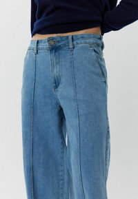 Svijetloplave traperice visokog struka s ravnim nogavicama, s prednjim džepovima i kontrastnim šavovima, izrađene od traper tkanine.