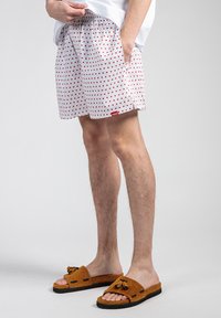 Hvite shorts med et rødt hjerte mønster, elastisk midjebånd, sidelommer, kombinert med brune sandaler med dusker.