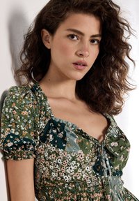 Blumenkleid mit Puffärmeln in Grün- und Pastellfarben. Verfügt über eine gebundene Front, eine geraffte Taille und verschiedene Blumenmuster auf weichem Stoff.