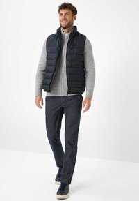 Dunkelblaue wattierte Weste über einem grauen Strickpullover mit gerippter Textur. Kombiniert mit dunkel gemusterten Hosen und navyblauen Sneakers.