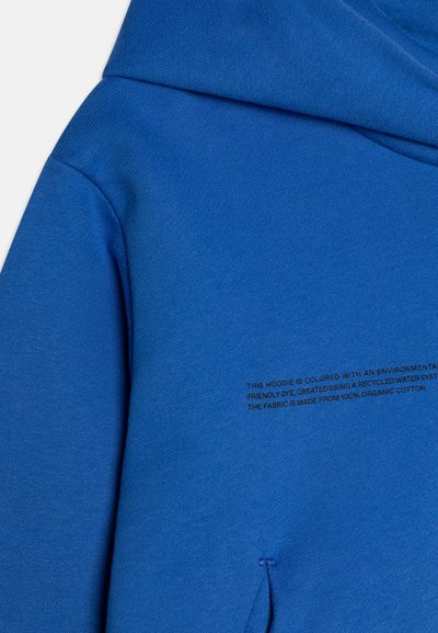 Hoodie w intensywnym niebieskim kolorze, wykonany w 100% z organicznej bawełny. Posiada fakturowaną powierzchnię oraz nadrukowaną metkę z instrukcją pielęgnacji z przodu.