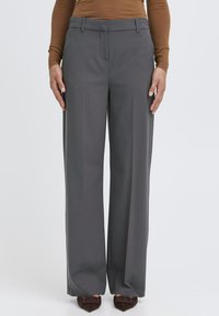 Šedé nohavice s priamym strihom a širokými nohavicami, hladkou textúrou a prednými vreckami, skombinované s hnedými lodičkami na vysokom opätku s mašľami.