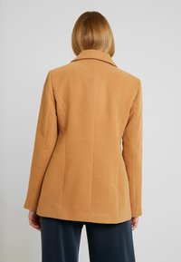 Kamelfärgad ullblandad jacka med skräddarsydd passform, slagkrage och slät textur. Har en enkel baksidedesign med vertikala sömmar.