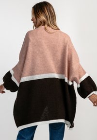 Przesadnie duży sweter dzianinowy w kolorze różowym, białym i brązowym. Posiada opuszczone ramiona, szerokie rękawy oraz luźny krój. Teksturowany materiał o luźnym splotie.