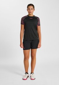 Czarna sportowa koszulka z różowymi rękawami w wzory, zestawiona z czarnymi szortami. Na koszulce i szortach widoczne różowe logo znanej marki.