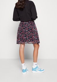 Blommig mörkblå kjol med en flödande design, tillsammans med ljusblåa och vita sneakers. Outfiten har en avslappnad svart topp.