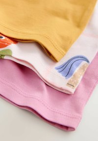 Trois t-shirts : le haut en jaune moutarde, le milieu avec un motif floral sur une base blanche, et le bas en rose clair. Tous fabriqués en coton doux.