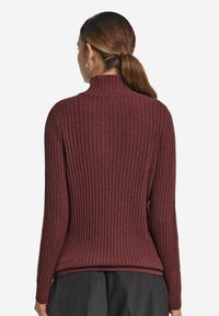 Ribbet turtleneck sweater i dyb burgunder. Har lange ærmer og en tætsiddende pasform, med struktureret stof og en let buet kant bagpå.