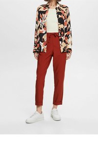 Koszulka w wielokolorowe kwiaty, jasna zielona bluzka i czerwone dopasowane spodnie z regulowanym paskiem; w zestawieniu z białymi trampkami. Gładki materiał i luźny krój.