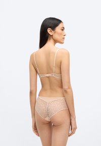 Σετ δαντελωτής γυμνής εσωρούχων με γεωμετρικό μοτίβο. Σουτιέν με ρυθμιζόμενες τιράντες και κούμπωμα με κράτημα. Συνοδευτικά διάφανα σλιπ τύπου hipster.