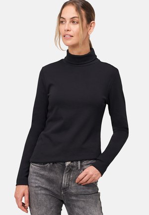 Haut noir à col roulé en tissu extensible avec des manches longues, présentant une silhouette ajustée et un design minimaliste. Porté avec un jean gris.
