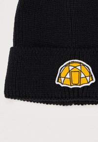 Gorro de malha preto com bainha dobrada, apresentando um design de iglu bordado em amarelo e branco na frente. Textura suave, forma versátil.