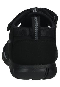Black sandals with a suede and mesh upper, adjustable strap, and a textured rubber sole. Back view shows a reinforced heel and gray stitching.