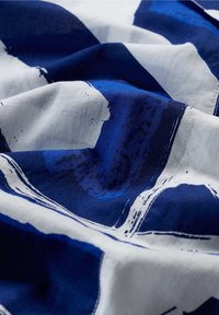Tessuto di cotone con motivi astratti in blu scuro e bianco, con texture visibile e una morbida caduta, che enfatizza il contrasto di colori e i dettagli delle pennellate.