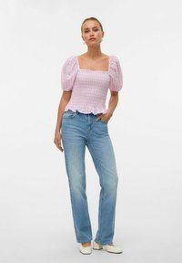 Rosa og hvit rutete smocketopp med puffermer og volangkant, parret med lyseblå rette jeans og hvite sko.