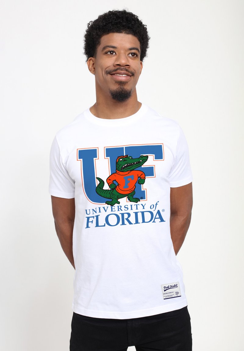 Hvid bomulds T-shirt med fede "UF" bogstaver i blå og orange. Inkluderer en grøn alligatorgrafik iført en orange trøje med teksten "University of Florida".