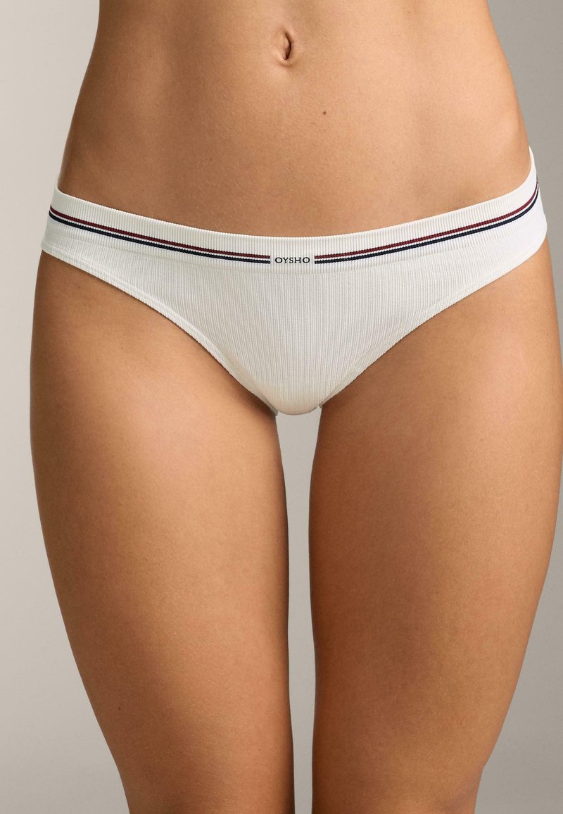 Culottes bikini en coton blanc côtelé avec une ceinture élastique rayée comportant des accents bleu marine et bordeaux. Logo placé au centre de la ceinture.