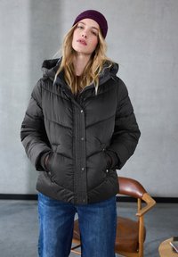 Puffjakke i sort med hætte, quiltet tekstur, knaplukning og sidelommer, sammen med blå jeans og en maroon hue.
