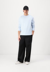 Light blue long-sleeve sweater, relaxed fit, round neckline. Paired with black wide-leg trousers and white sneakers. Black cap accessory.