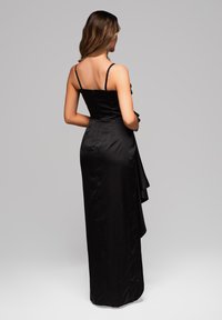 Svart aftonklänning gjord av silkesliknande material, med en figursydd bodice, tunna axelremmar och en sväva kjol med en volangöverdrag bak.
