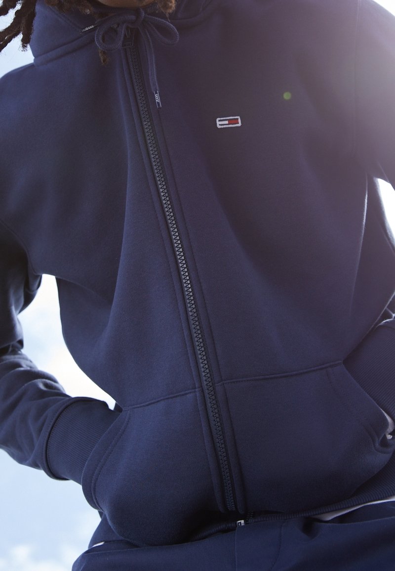 Felpa con zip di colore blu navy realizzata in un tessuto morbido, dotata di un piccolo logo ricamato sul petto e di cordini sul cappuccio.