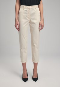 Beige cropped trousers made of smooth fabric, featuring a high waist, slant pockets, and a straight leg design, paired with black heels.