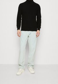 Suéter negro de canalé con cuello alto combinado con jeans rectos de pierna clara y zapatillas blancas, con un diseño casual pero ajustado.