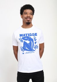 Bílá tričko s výrazným modrým grafickým potiskem sedící postavy, s textem "MATISSE" a detaily umění, krátké rukávy, kulatý výstřih.