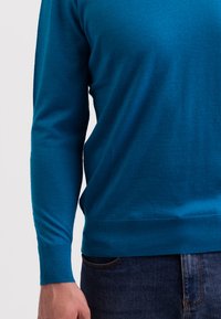 Modrý pletený svetr s dlouhými rukávy, žebrovanými manžetami a lemem. Hladká textura, přiléhavý střih, spárovaný s tmavě modrými džínami.