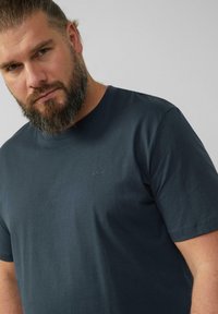 Camiseta de algodón azul marino con mangas cortas, que presenta un pequeño y sutil logotipo bordado en el pecho. Textura suave, diseño de cuello redondo.
