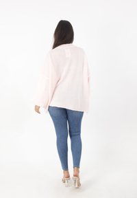 Jasnoróżowy, oversize'owy sweter z długimi rękawami, teksturowany materiał, o okrągłym dole, zestawiony z niebieskimi rurkami i przezroczystymi sandałami na obcasie.