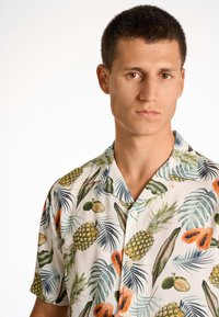 Kortærmet knap-op skjorte med en lys baggrund og et tropisk print af ananas, papayaer og grønne blade. Blødt stof.